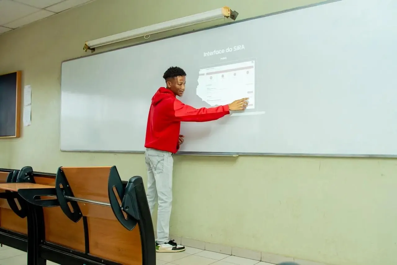 Adilson Muffins aponta para o painel projectado com o título “Interface do SIRA”, numa sala de aula.